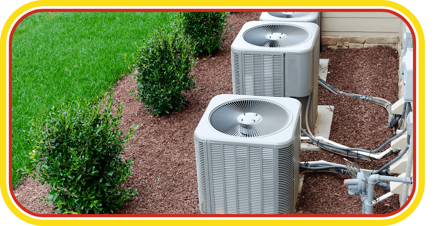Outdoor air conditioner units beside a landscaped lawn and shrubs