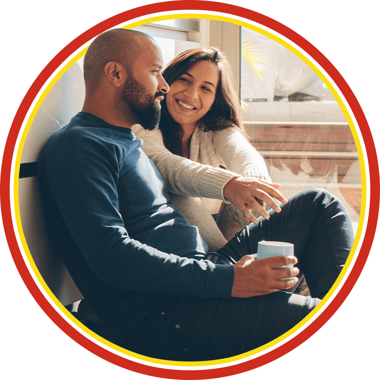 Smiling couple cuddling on a couch in warm light, holding a mug